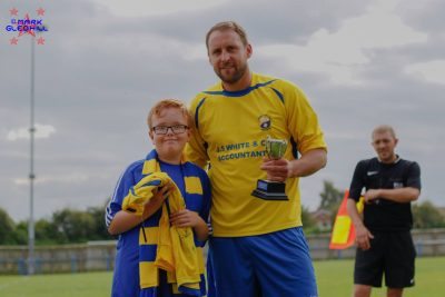 Garforth Town Legends captain Brett Renshaw collects the Ralph Backhouse Trophy from Ralph's great nephew Jack Yelland and presents him with a signed Miners jersey by the players involved in the game